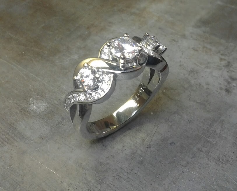 custom designed white gold engagement ring with swirled band and triple set diamonds side view